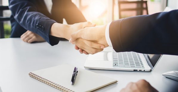 People shaking hands over a table with a notebook and a laptop