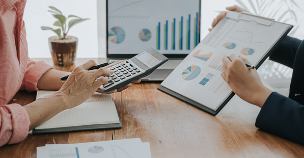 Image of two people collaborating with a calculator and clipboard of financial data charts