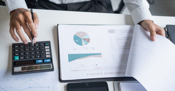 Stock image of person working on a calculator and looking at a clipboard with data and models