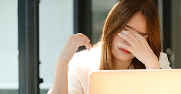 A woman working at a laptop appearing to be stressed