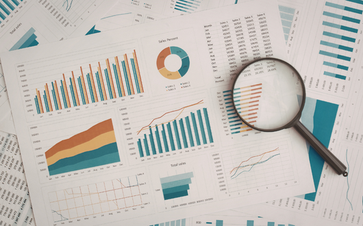 magnifying glass laying on top of several papers with charts and graphs