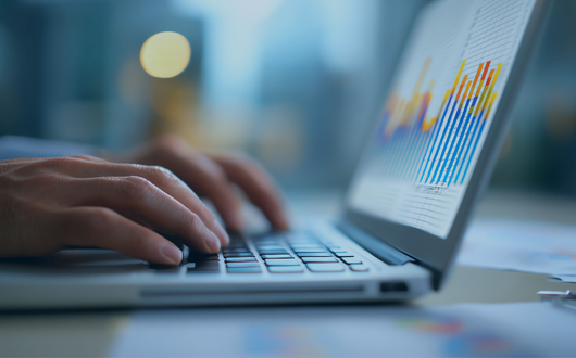 a person typing on a laptop with charts on the screen