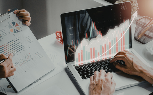 Person looking at digital reports on a computer and another person showing them a paper report