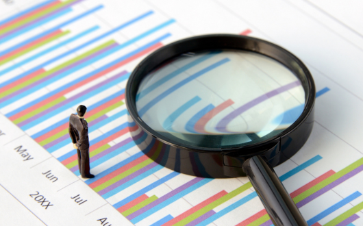 Stock image of a small person figure on top of a paper with a graph and a large magnifying glass