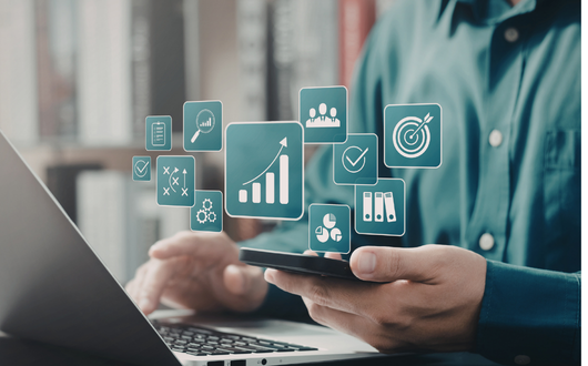 A person looking at a laptop and a phone with digital symbols coming out of it