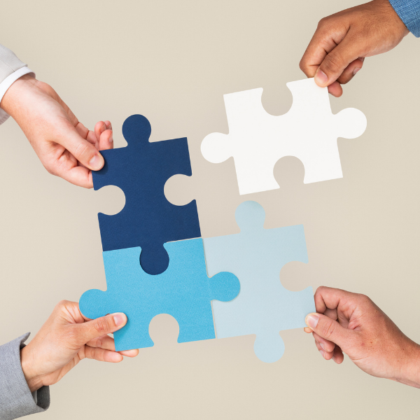 Overhead view of four hands fitting large puzzle pieces together