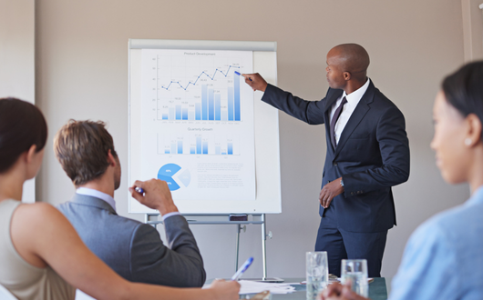 A person standing in front of people, presenting a report of analytics