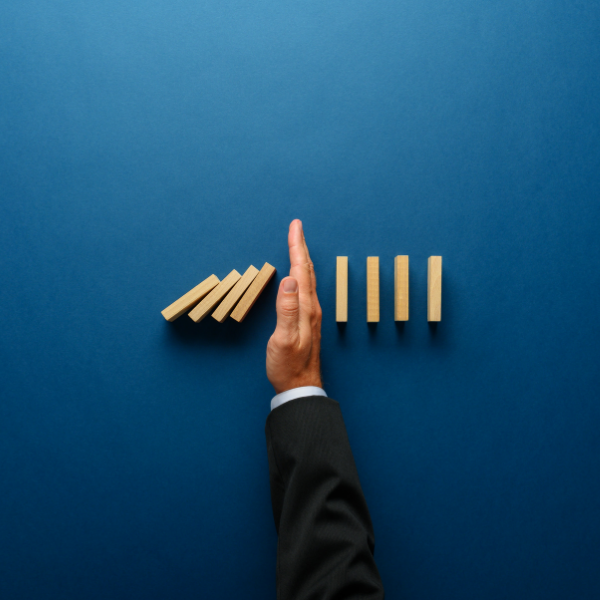Stock image of a persons hand interrupting a chain of falling dominos