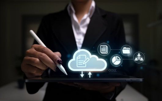 Photo of a person using a stylus pen to click something on a decide with a cloud icon and other digital symbols coming out of it